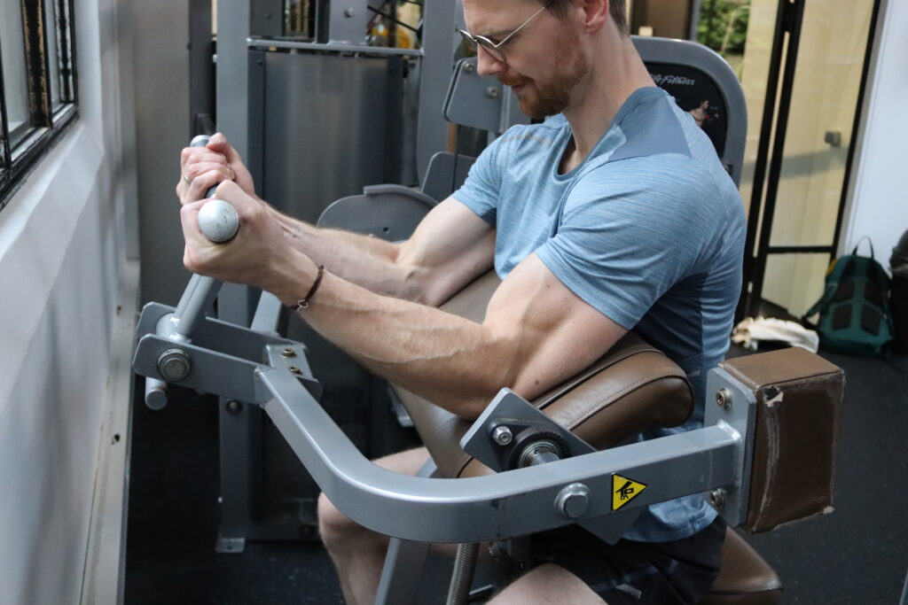 Personal trainer Wijnand Dijkshoorn voert de machine curl uit in sportschool Ceder Gym in Den Haag